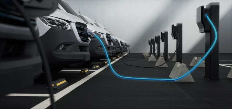 Fleet of generic electric EV delivery vans charging on charging stations